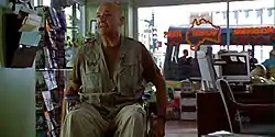 A bald man in a wheelchair, inside a travel agency.