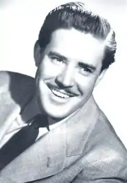 Black-and-white photo of smiling, mustachioed man in a suit