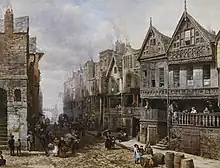 A street in the 19th century with buildings on the left, the first of which is timber-framed and highly decorated. In front of the house is a horse and cart