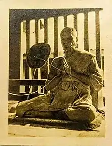 Elderly monk in gesture of prayer, with a thread wrapped around the palms of his hands.