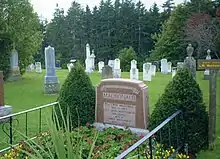 The gravestone of Montgomery, in a grassy cemetery. The text on the gravestone says, "Lucy Maud Montgomery Macdonald/wife of/Ewan Macdonald/1874–1942.