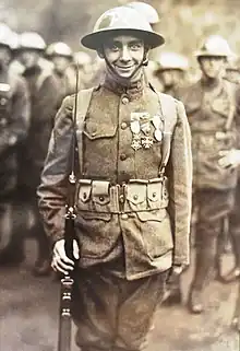 Three-quarters frontal picture of a man in uniform wearing a metal helmet with 2nd Infantry Division insignia.  The Medal of Honor, French Croix de guerre with two bronze palms and one silver star and Montenegrin Medal for Military Bravery are pinned to his uniform coat.