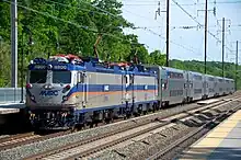 A large commuter train with blue and orange stripes sits at a train station.