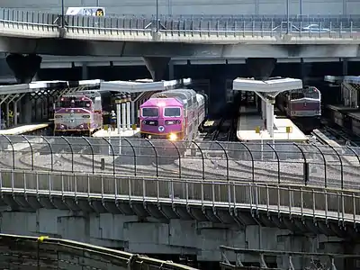 A diesel locomotive with a passenger train leaving a station with several tracks and high-level platforms