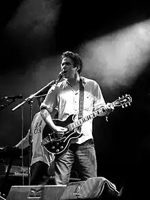 A black and white photo of a man playing guitar on a stage