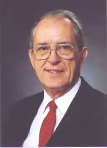 image of Mack Breazeale from 1997, smiling in a white shirt, red tie, and dark suit coat