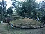 Several tumuli in a forest, tourists walking around