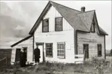 Two men in cassocks in front of a house.