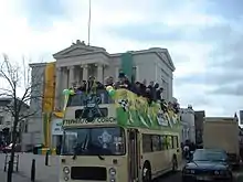 A group of men are standing on the top level of a double-decker bus.