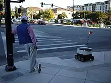 Image 72A man and a delivery robot waiting at a pedestrian crossing in Redwood City, California, United States. E-commerce spurred advancements in drone delivery and transformed parts of the services and retail sectors (from 2010s)