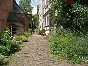 A pocket park in Marburg, Germany features a cobblestone walking path, flower beds, and a sitting area.