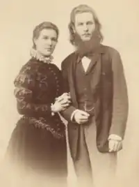 Portrait of a standing woman in Edwardian dress holding the arm of a standing bearded man.