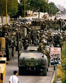 Many soldiers and military vehicles near a vandalized road sign