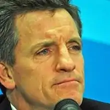 A head shot of a middle-aged white male. A microphone is in front of his face.