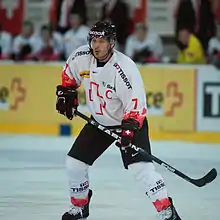 A Caucasian male ice hockey player shown from the knees up. He is wearing a red and white sweater with a black helmet.