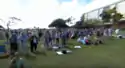 People stand and sit on a green lawn before a sunny sky.