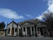 Features three concrete mausoleums with ornate columns and peaked roofs..