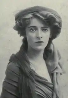 Head and shoulders of a woman with dark hair, wearing a draped dress and flat hat