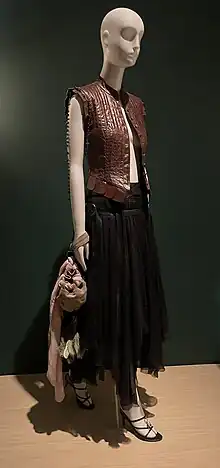 A sleeveless leather vest, black ankle-length skirt, heeled shoes, and a purse on a mannequin