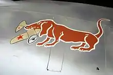 A painting of a dachshund holding a Soviet aircraft in its mouth.