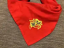 A photo of a Red Scout Scarf with an embroidered gold emblem