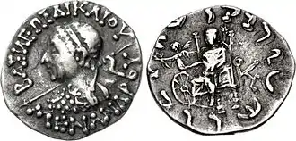 Coin of Menander II (90–85 BCE), with seated Zeus and Nike on his arm, extending a victory wreath over a wheel symbol