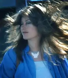 Head and shoulders of a woman with long brown hair spinning around, wearing a blue top in soft focus