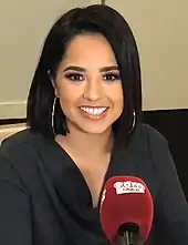 Becky G smiles into a large, red microphone.