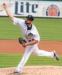 A man in a white baseball uniform and a black cap