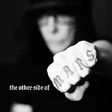 A blurry, black-and-white photo of the artist, with the camera focused on his fist in front of him displaying the word "MARS" tattooed on his knuckles.