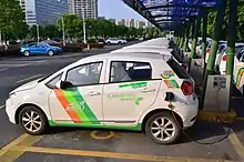 Photograph of a row of cars plugged into squat metal boxes under a roof