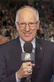 Mike Emrick smiling while holding a microphone in his right hand