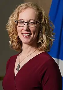 The official portrait of Minister Lorna Slater. She has blonde curly hair, and is smiling. In the background, a Scottish flag can be seen.