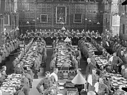 Photograph of a group of officer cadets and waiters in army uniform during a dinner service in a formal hall