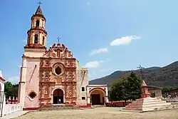 Facade of a church with one tower. The main portal is richly decorated with relief and sculptures and features a clock at the top.