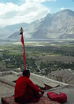 A monk meditates on the terrace of Diskit Monastery, with the Nubra Valley and the Diskit village seen in the background