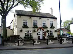 A cream-coloured public house with window boxes in front of which are picnic-type tables.