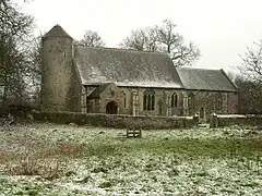 A mainly stone church with a round tower on the left, to the right is a nave with a porch, and a chancel at a lower level