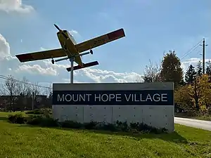 Sign of Mount Hope with a Beechcraft CT-134 Musketeer mounted next to it.