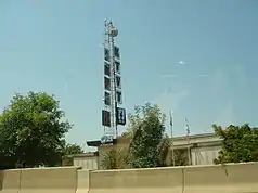 A one-story building with a microwave tower on which five square signs are hung, with the letters K, T, V, and T, and the CBS 11 logo. A smaller UPN 21 sign adorns the front of the building.