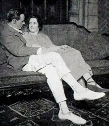 stage scene: a young white man in sports jacket and flannels, on a sofa with a young woman; they are gazing lovingly into each other's eyes