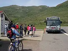 A bus in a parking lot, with grassy hills in the background