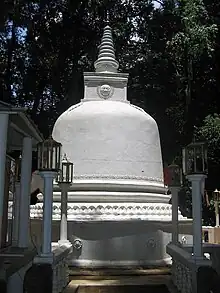 The white coloured stupa of Na Uyana Aranya is in the foreground. Tall Ceylon ironwood trees, which has given the monastery its name, can be seen in the background.