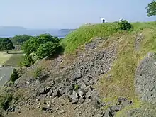 Hill with remains of stone foundations. In the distant background there is the see.