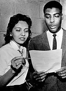 A man and woman look over a document the man is holding. The woman points to a particular section with a pen.