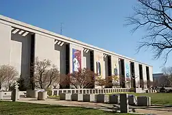 An oblique view of a white stone modernist building. The facade steps forward and then back 9 times, spread out equally across its front.