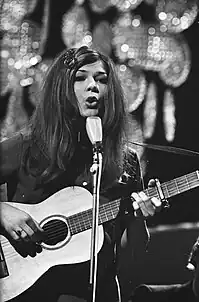 Black-and-white photograph of Lenny Kuhr performing on stage in 1969 with guitar and mic stand.