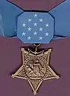 A light blue neck ribbon with a gold star shaped medallion hanging from it. The ribbon is similar in shape to a bowtie with 13 white stars in the center of the ribbon.