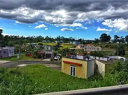 Clouds above a blue sky, curvy road, colorful cement homes and greenery