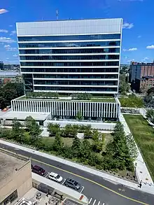 A picture of glass skyscraper with a white facade that is 10-15 stories tall, taken from another nearby tower.